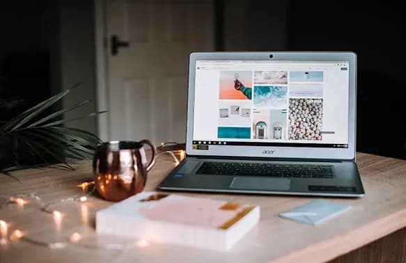 A laptop open on a desk beside a mug and fairy lights